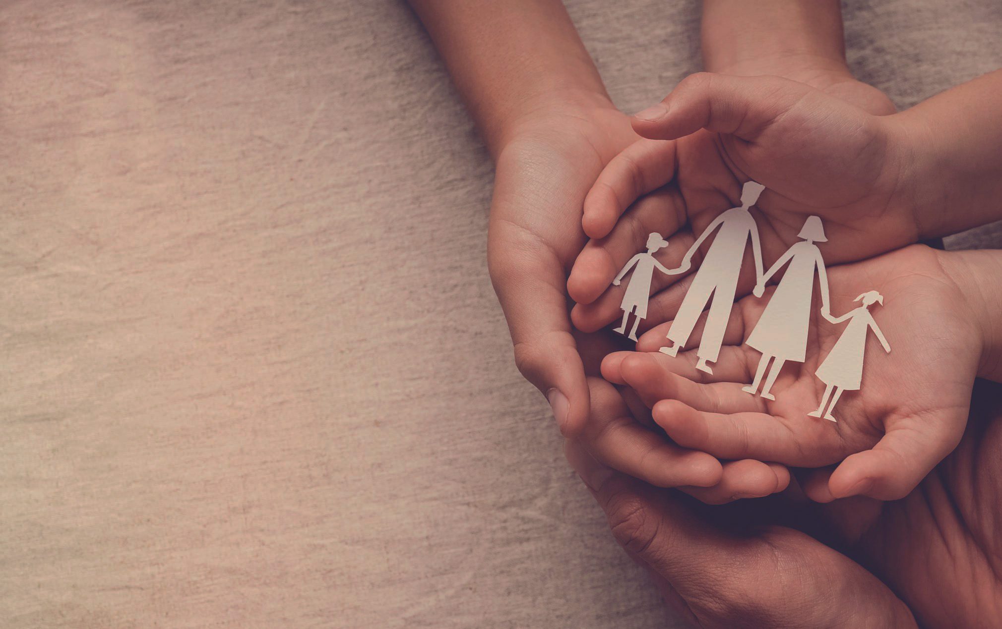 Two pairs of hands holding a paper cutout of a family