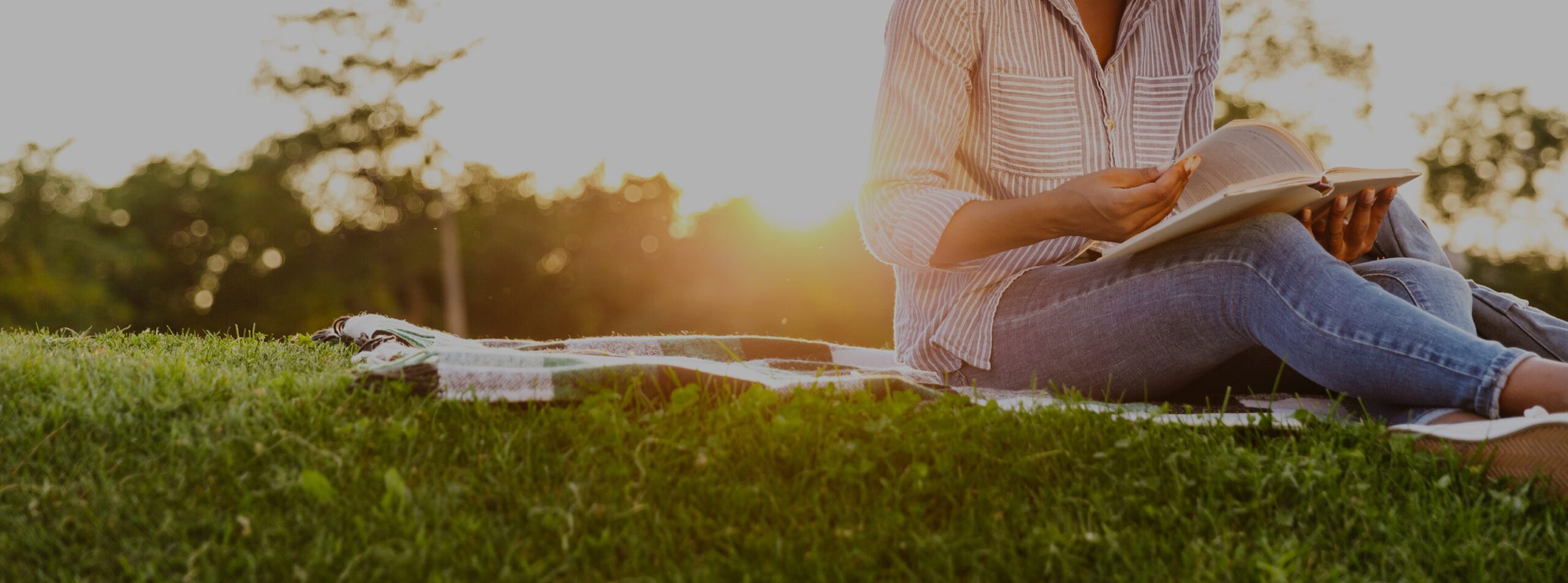 Woman sitting outside, reading on the grass at sunset